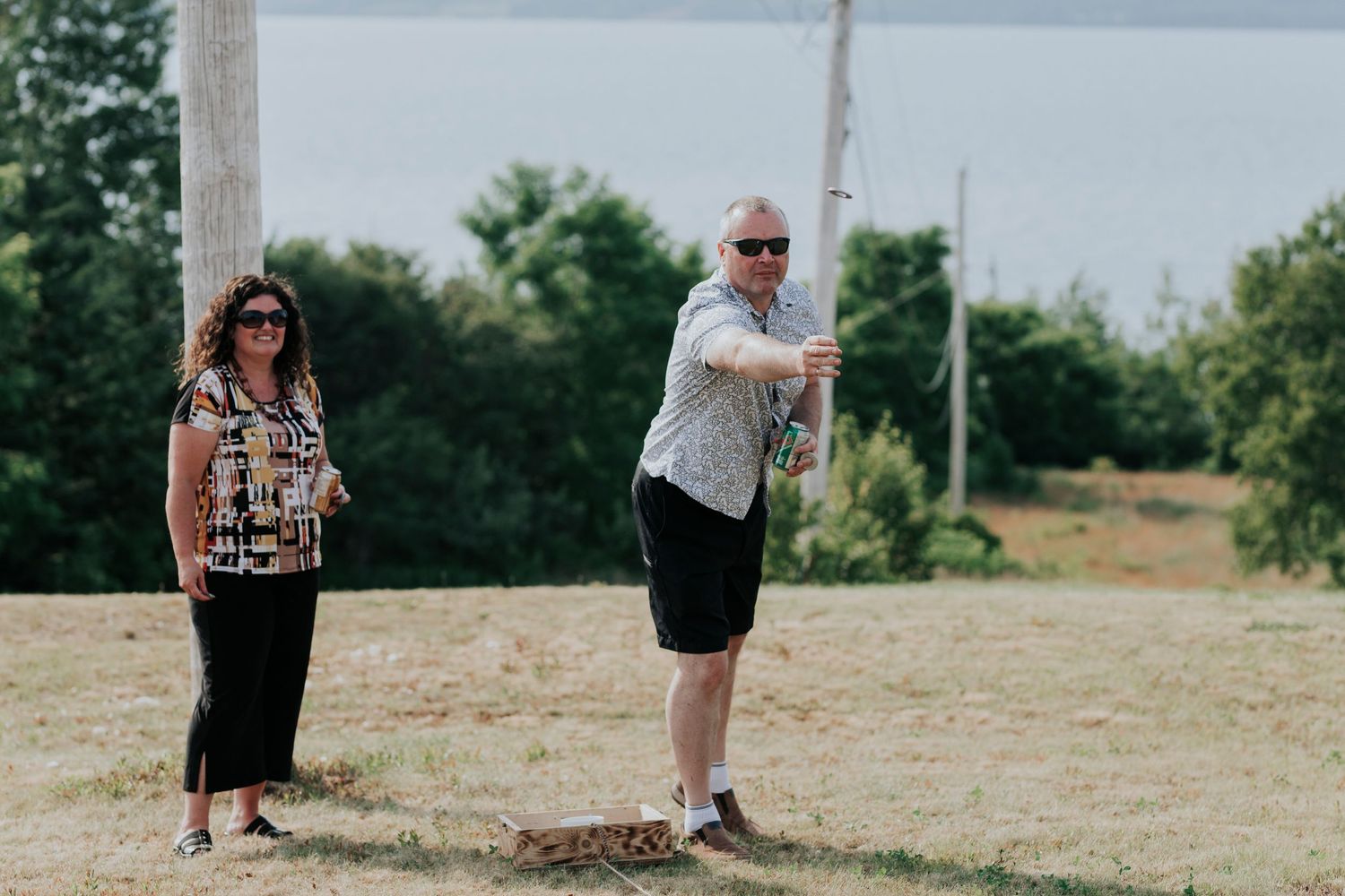 Two people stand in a grassy field on a sunny day, with one person gesturing while the other watches.