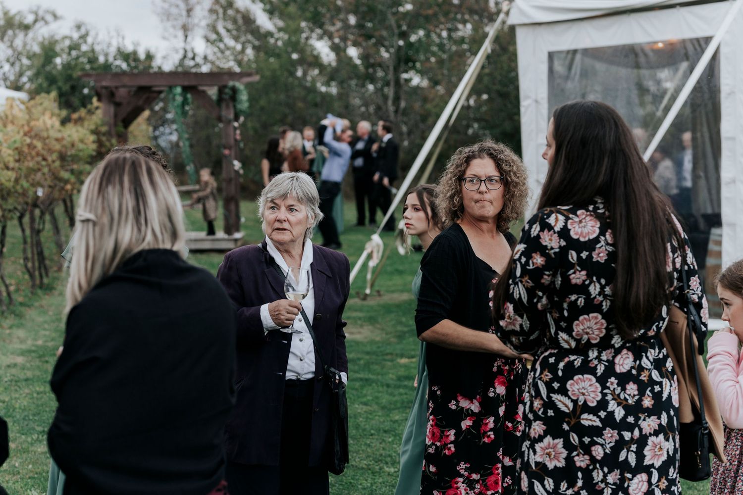 Wedding guests mingle during outdoor reception on grassy lawn.