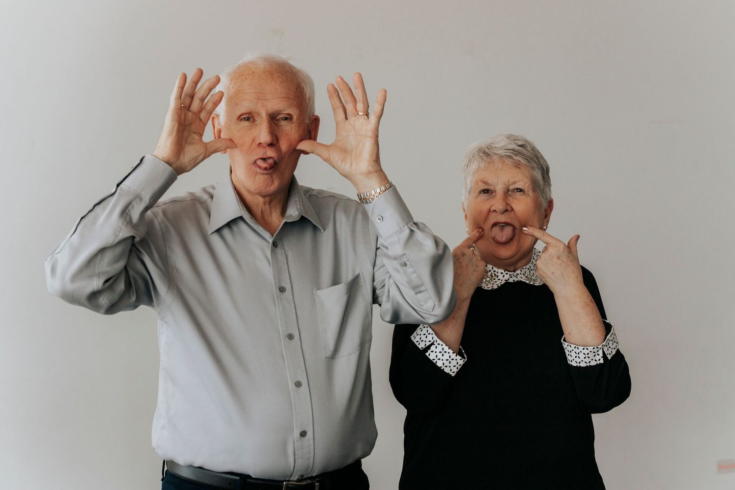 Playful elderly couple making funny faces against white background, sticking tongues out.