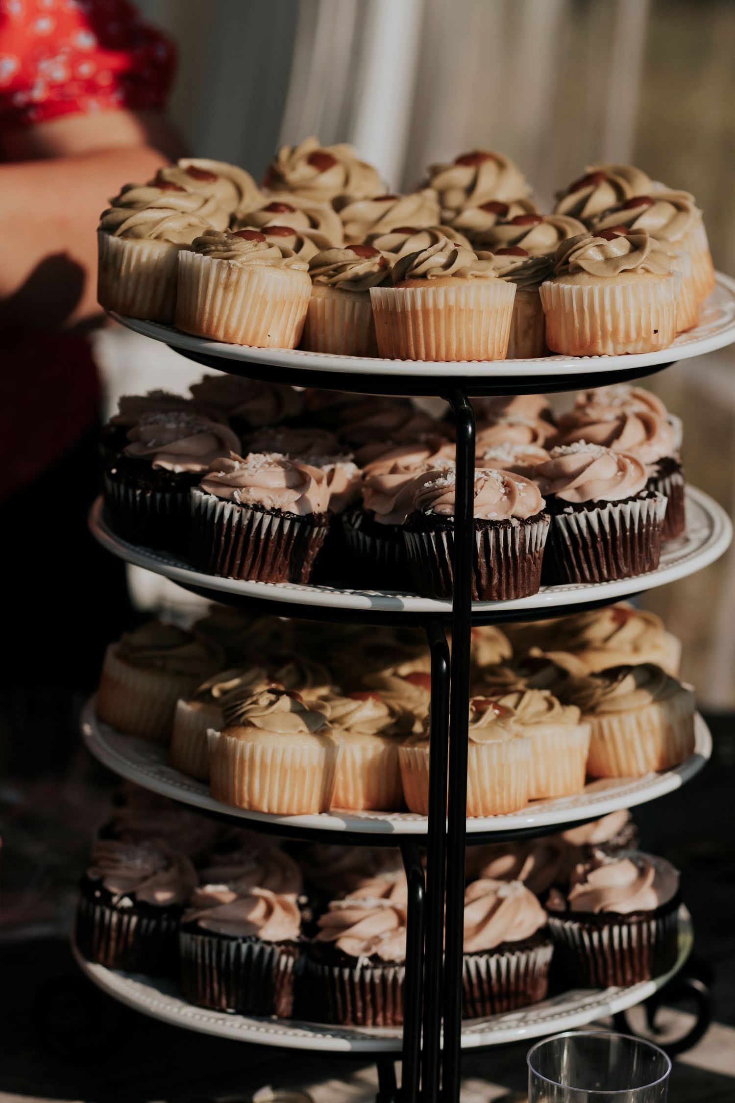 A tiered dessert stand displays an assortment of chocolate and vanilla cupcakes with swirled frosting drizzle.