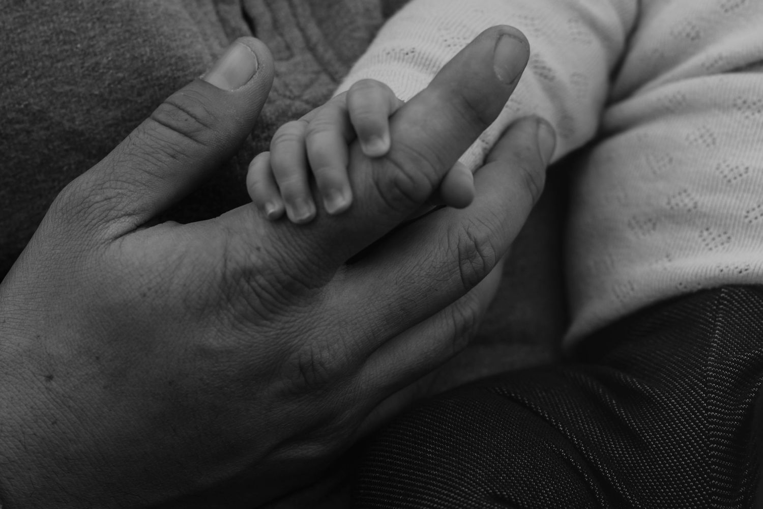 Black and white close-up of a newborn baby holding an adult finger in a tender moment.