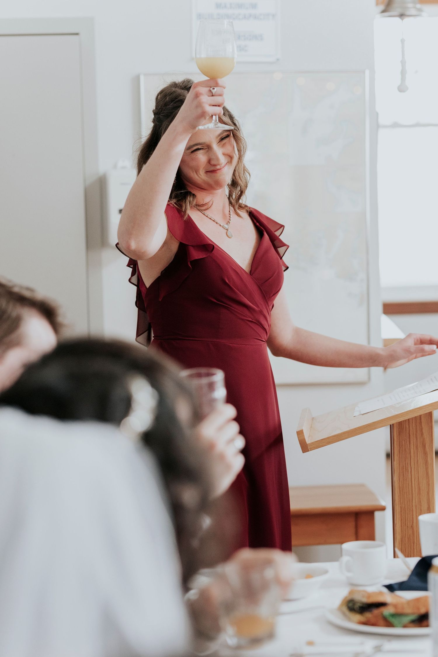 Someone in a burgundy wrap dress raises a champagne glass in celebration during what appears to be a social gathering.