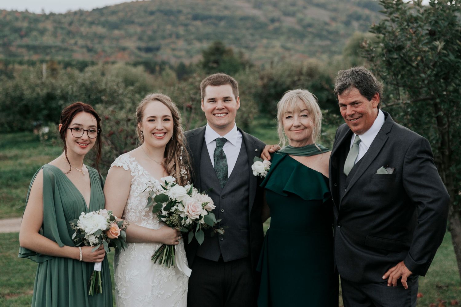 Small wedding party group poses outdoors with mountain vista behind them.