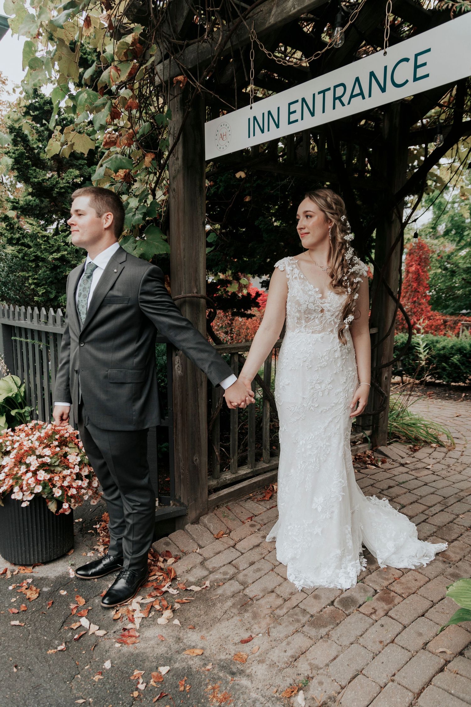 Couple poses holding hands at rustic inn entrance with fall decorations.