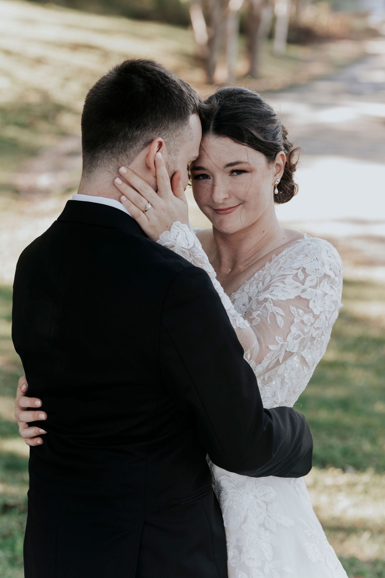 A tender wedding moment captured as a bride and groom embrace outdoors in natural lighting.