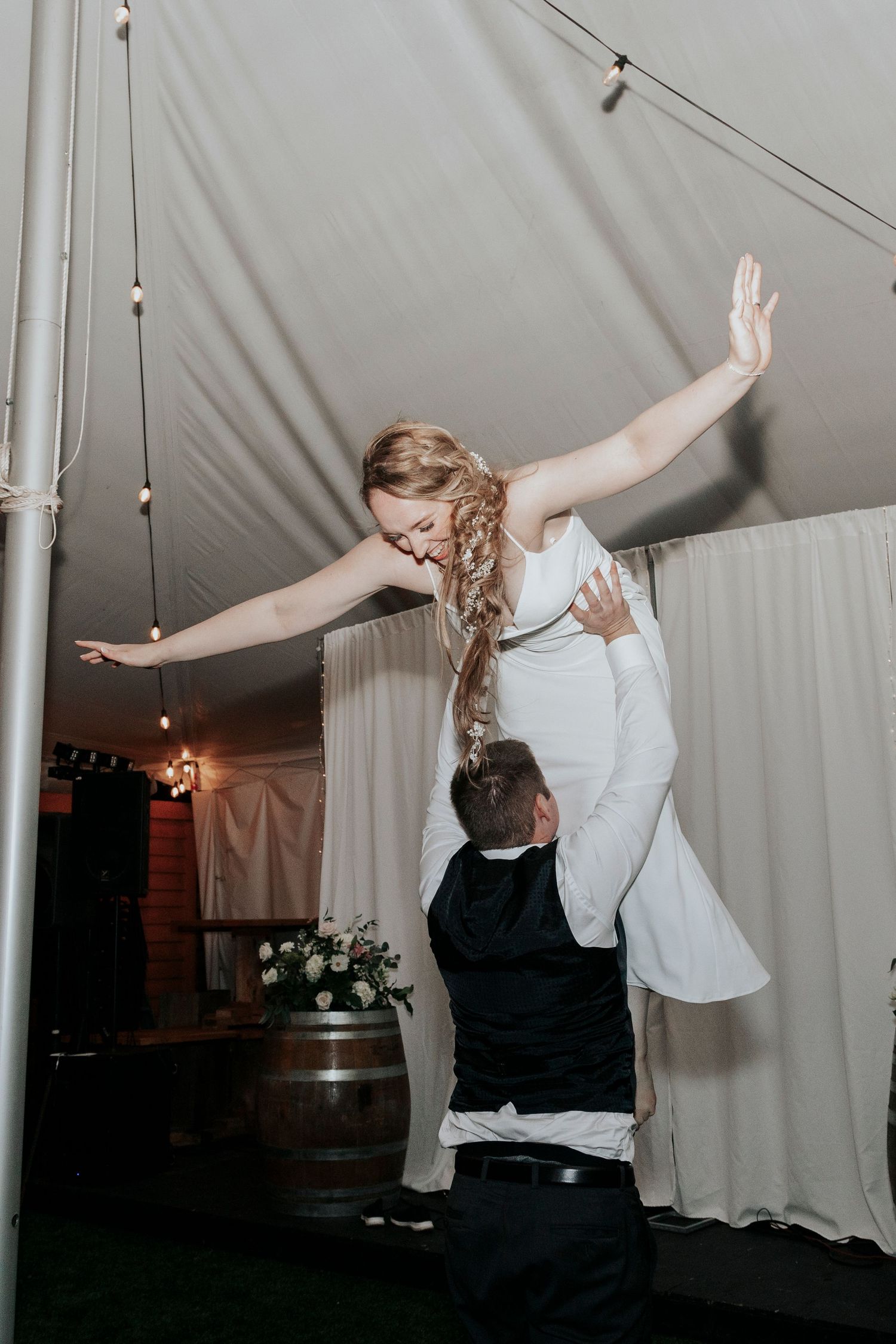 A couple performs a dramatic lift during their wedding dance under string lights in a tented reception venue.