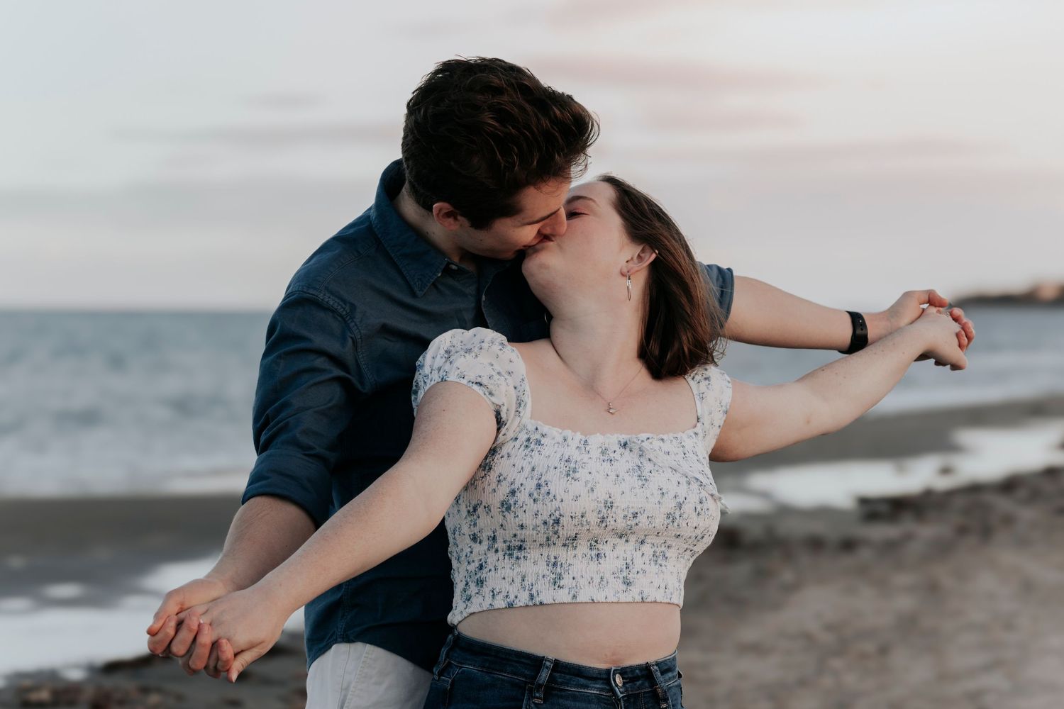 Couple sharing a romantic dip kiss on the beach at sunset during engagement photo session.