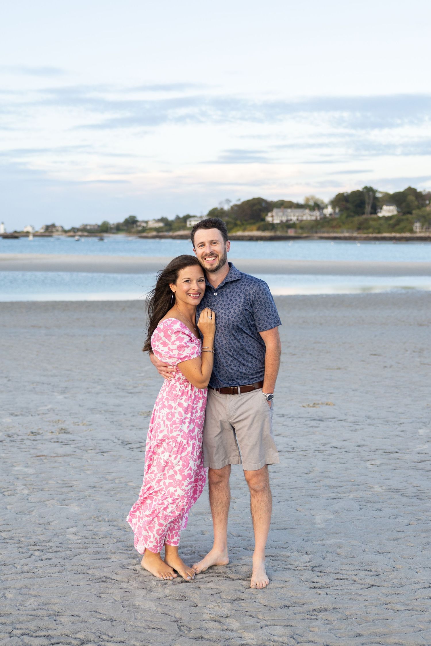 Smiling couple embracing barefoot on sandy beach at sunset in coastal New England.