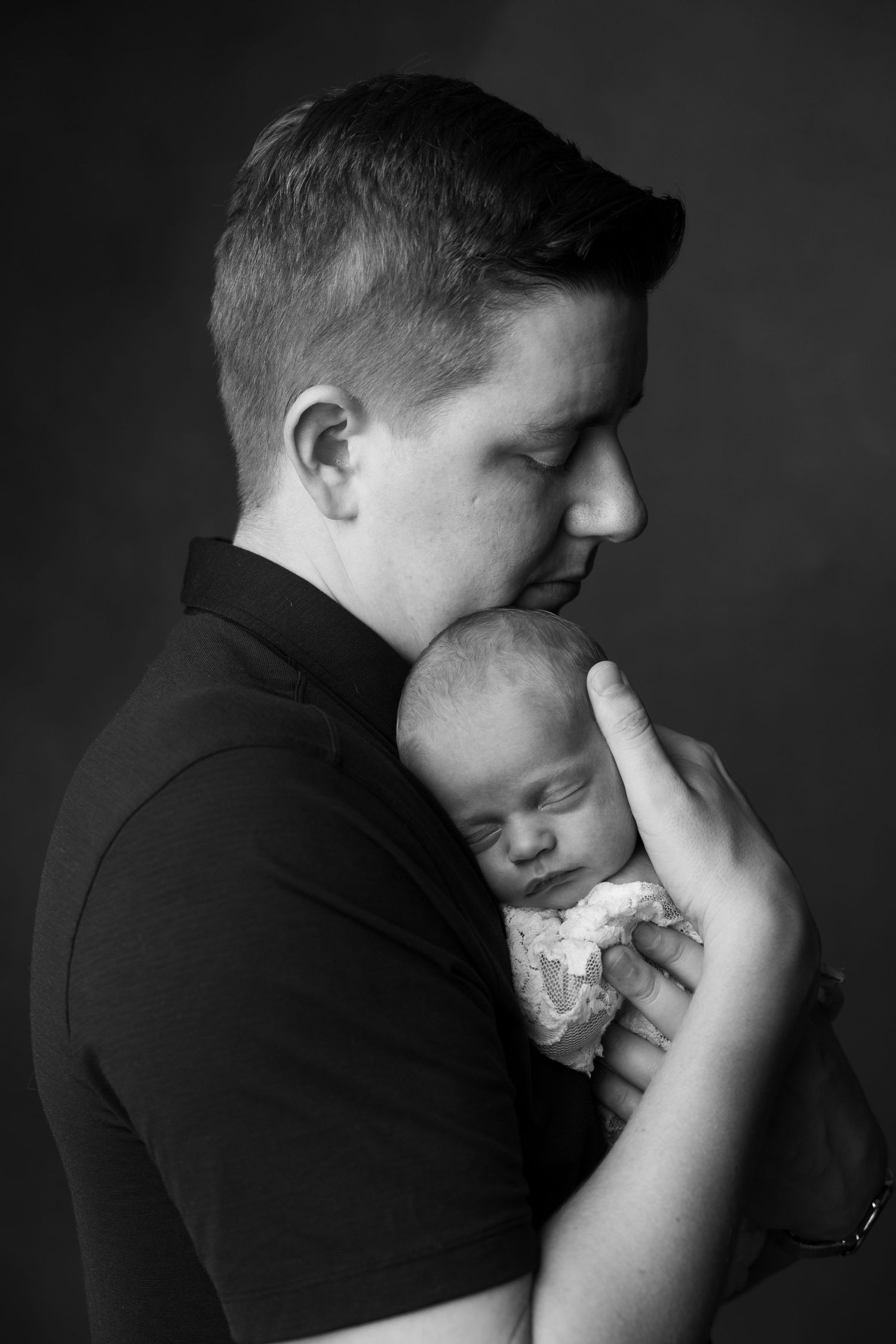 Black and white portrait of a father tenderly holding his sleeping newborn baby close to his chest.