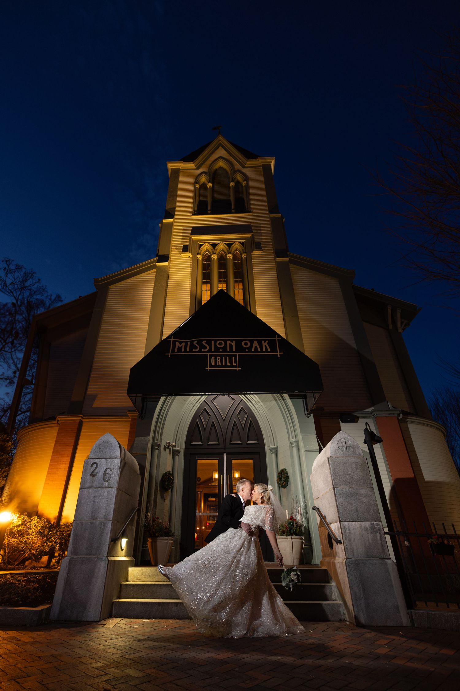 Bride and groom share romantic kiss at night outside Mission Oak Grill, a stunning church-style wedding venue.