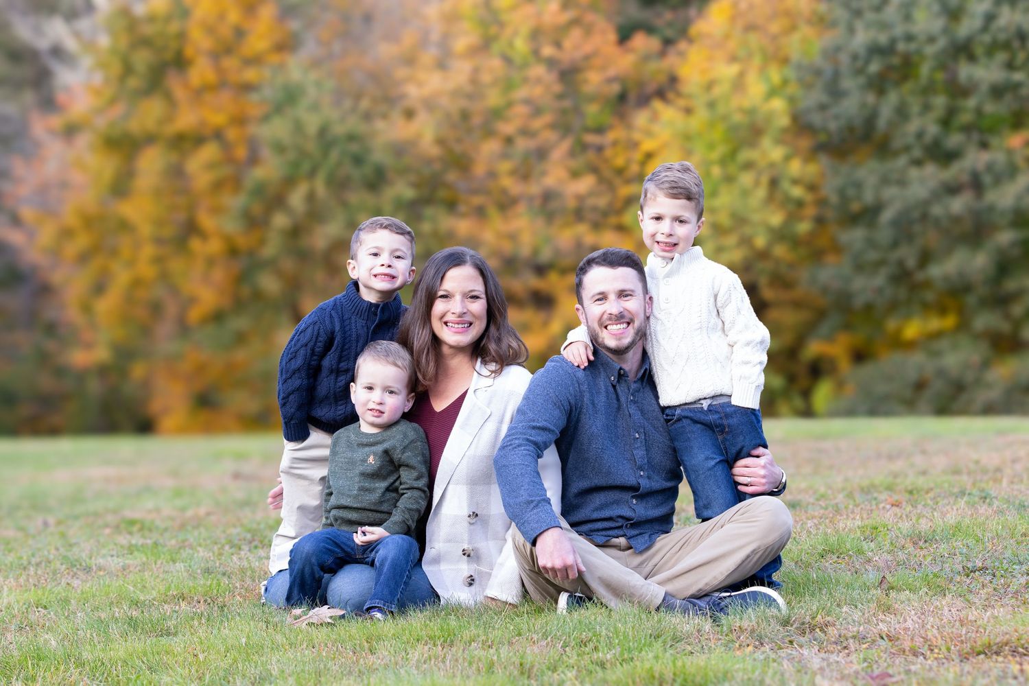 Family of five posing outdoors in autumn park with colorful fall foliage trees in background.