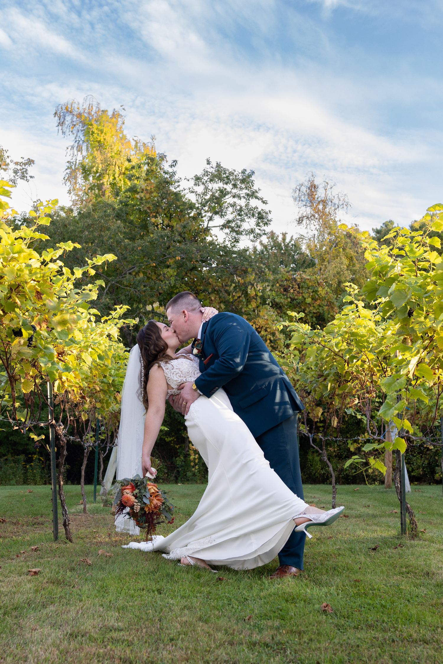 Bride and groom share a romantic dip kiss in a lush vineyard setting on their wedding day.