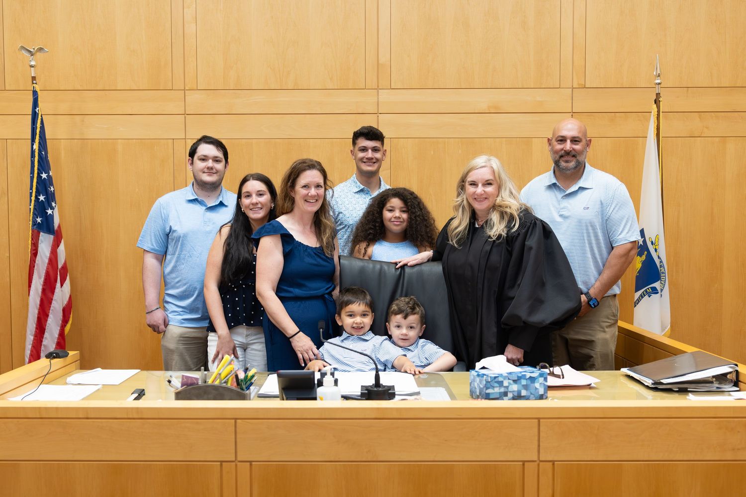 Family poses with a judge in black robes at a courtroom bench with an American flag during a legal ceremony.