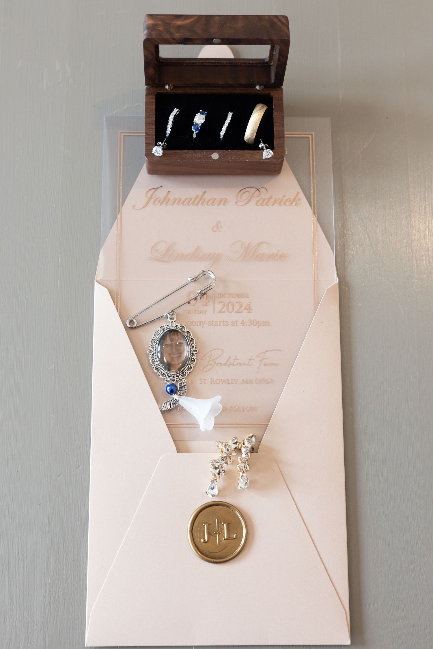 Elegant wedding flat lay with engraved invitation, jewelry, brooch, and ring box displaying wedding bands.
