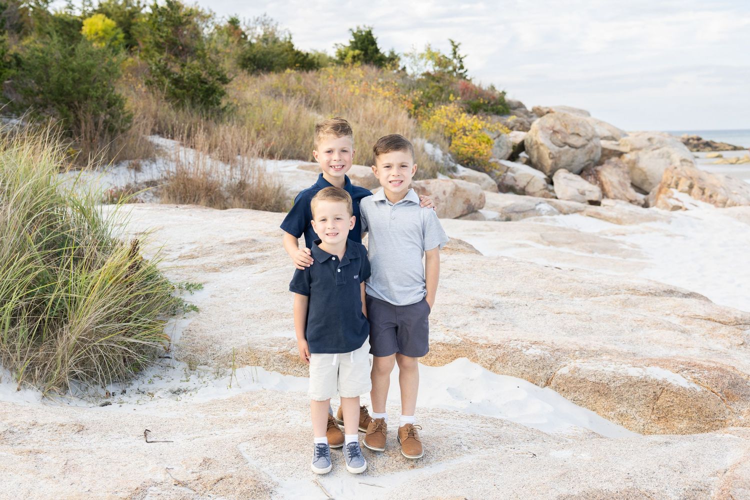 Three brothers posing together on rocky New England beach on a sunny day.