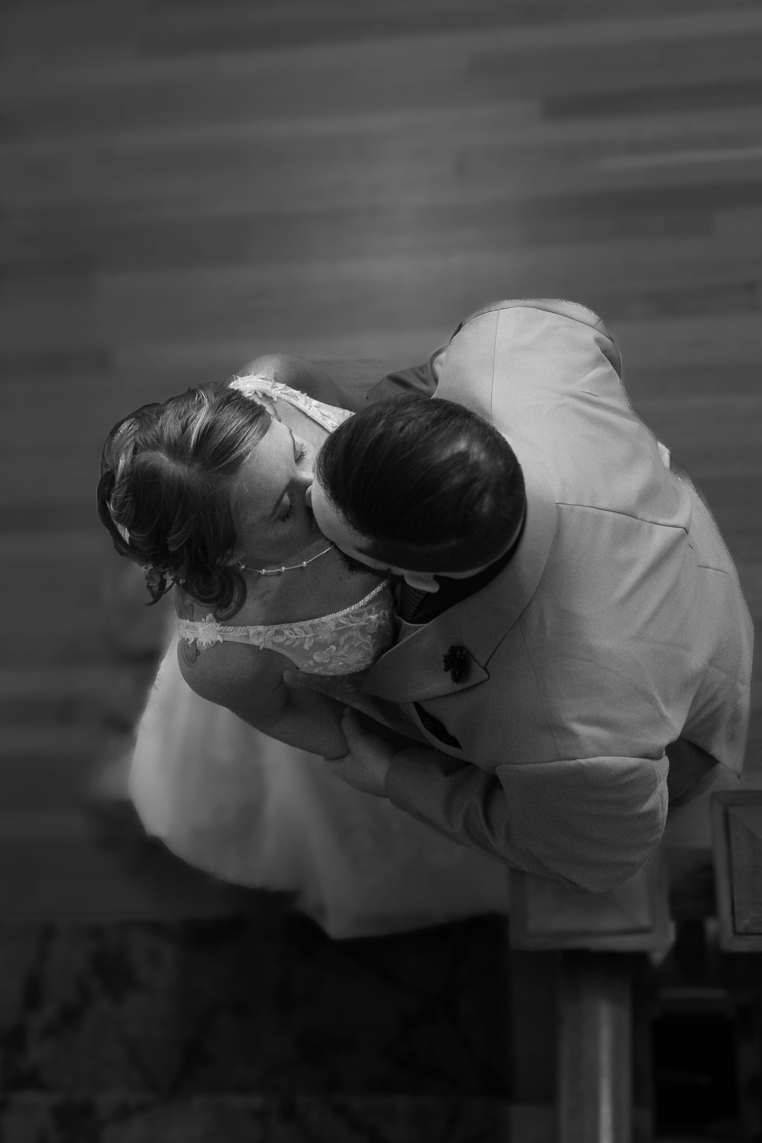 Aerial black and white photo of a bride and groom sharing a kiss during their wedding ceremony.