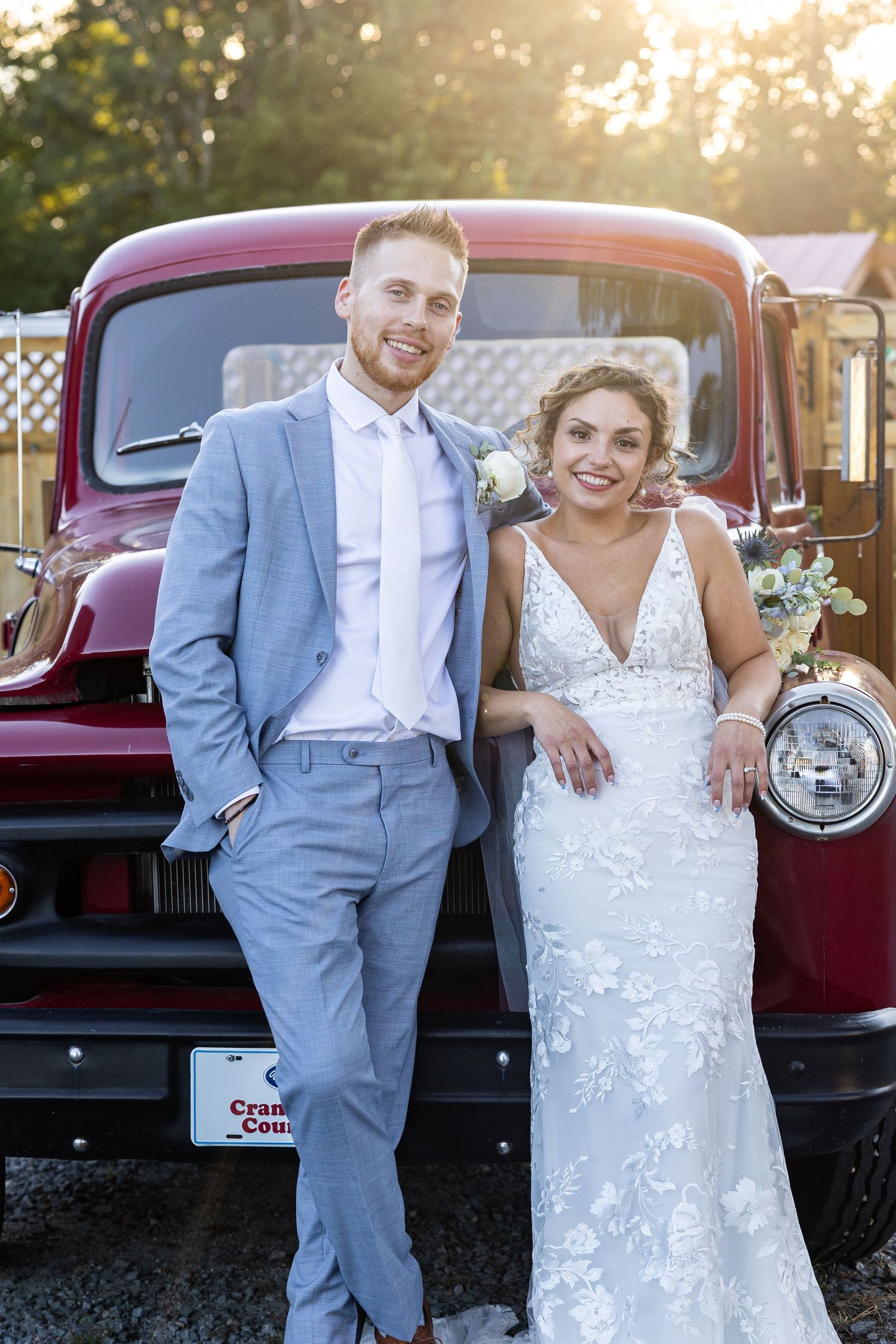 Bride and groom smiling in front of a vintage red truck on their wedding day.