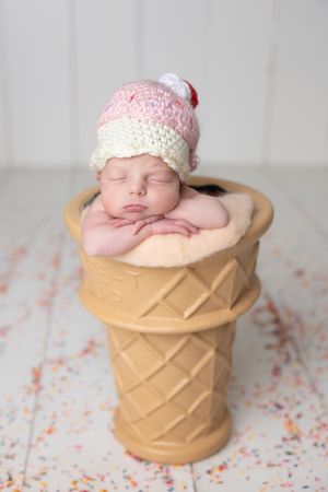 Adorable sleeping newborn baby posed in an ice cream cone prop wearing a pink knit hat.