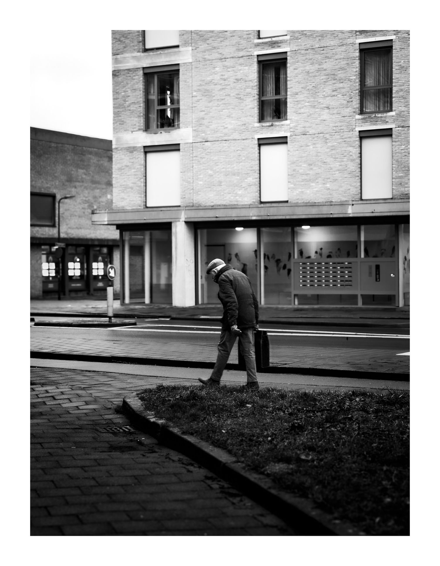 Man walking alone on urban street beside brick building, black and white photography.
