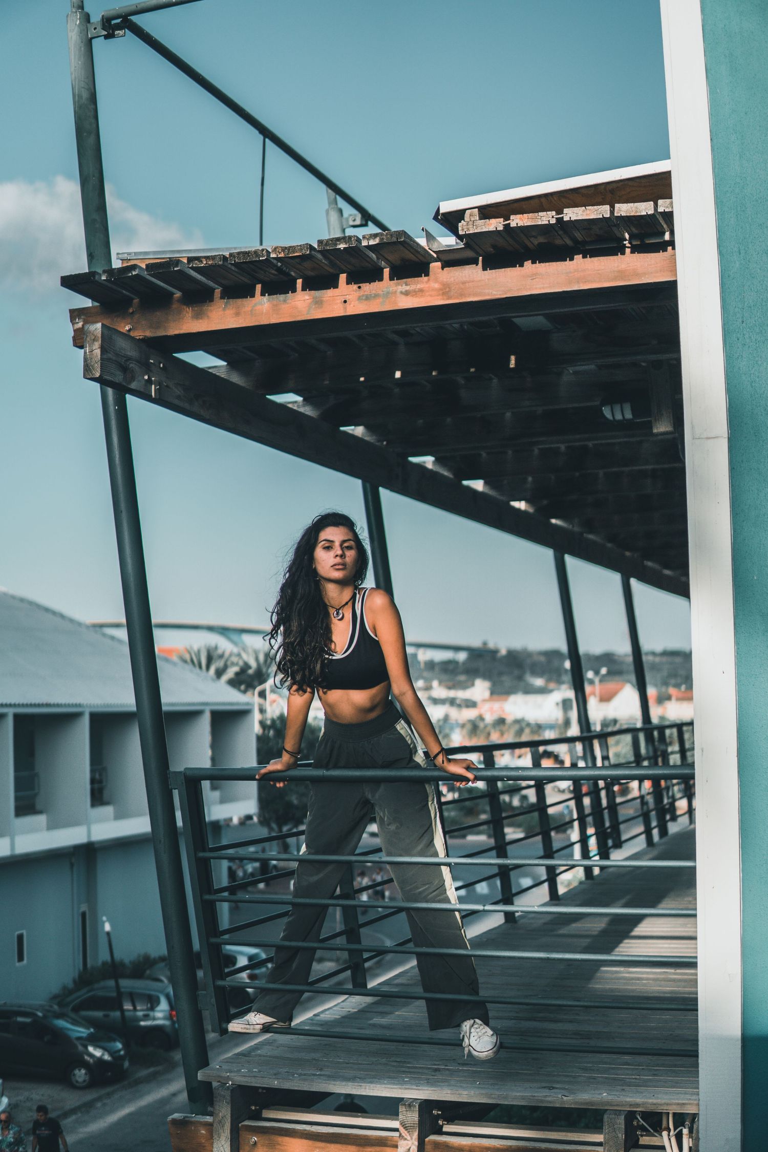 Athletic woman in black sports outfit posing on a rooftop deck with city views behind her.