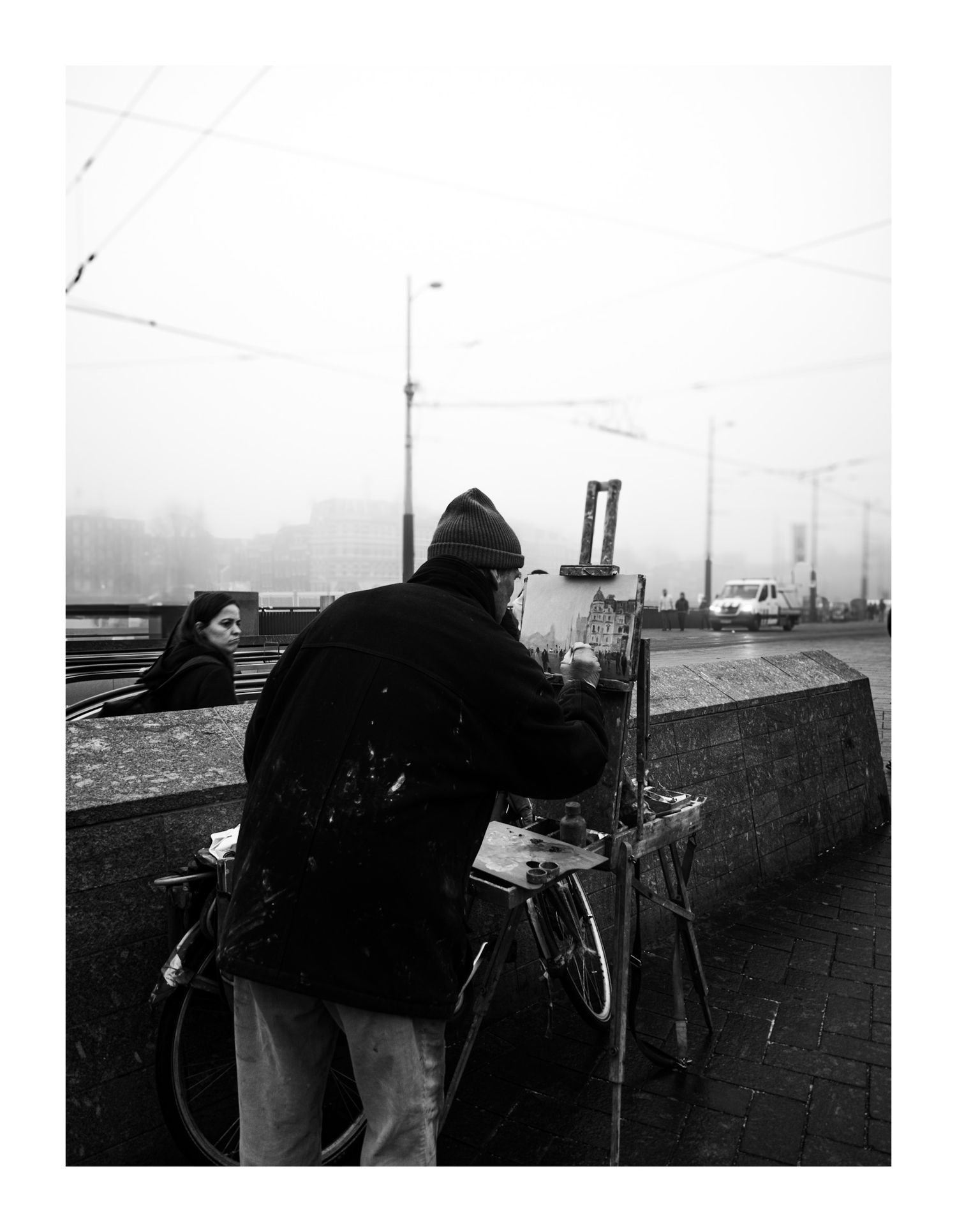 Street artist painting on easel in foggy urban setting, black and white photography.
