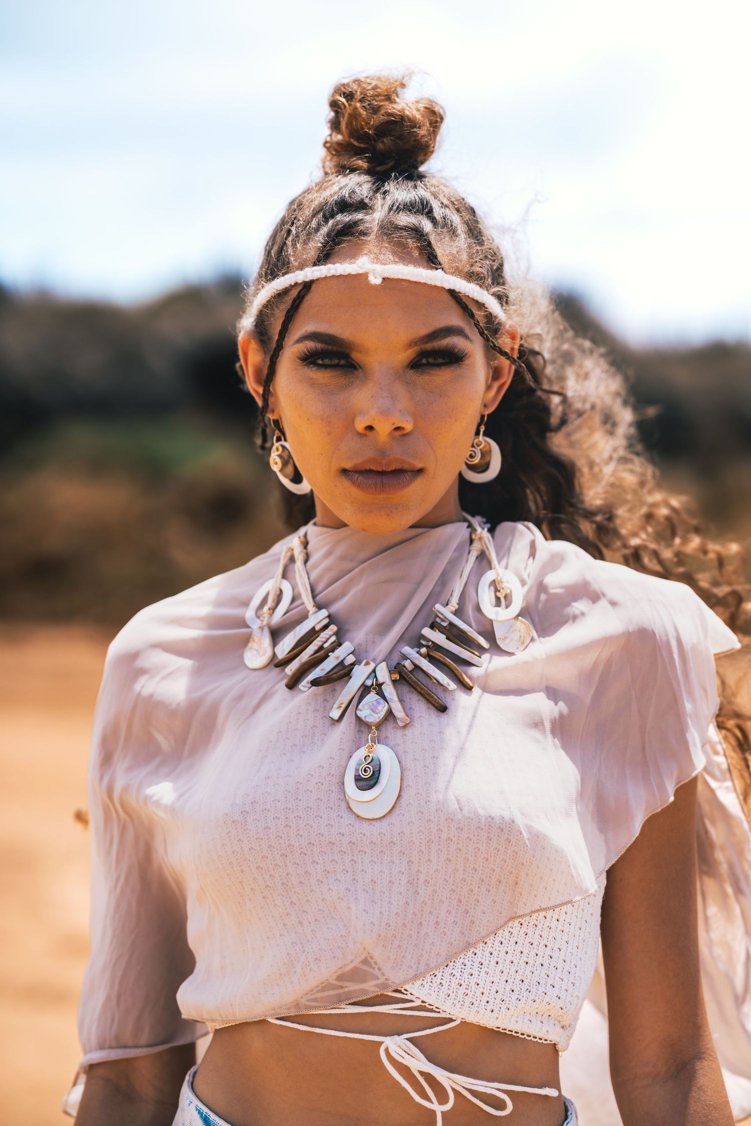 Close-up portrait of woman wearing shell necklace and headband in desert setting.