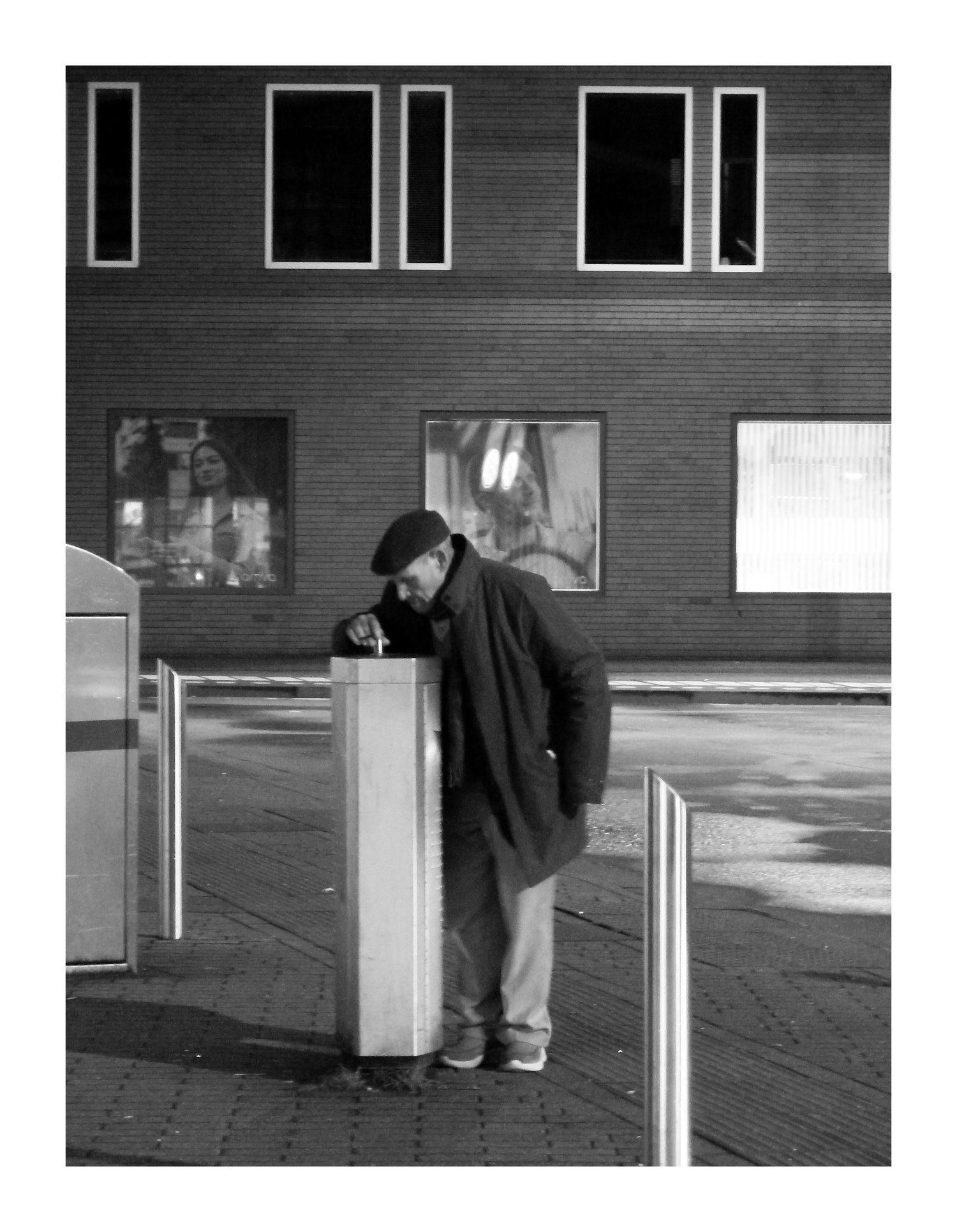 Man leaning over street fixture at night on empty urban street, black and white photo.