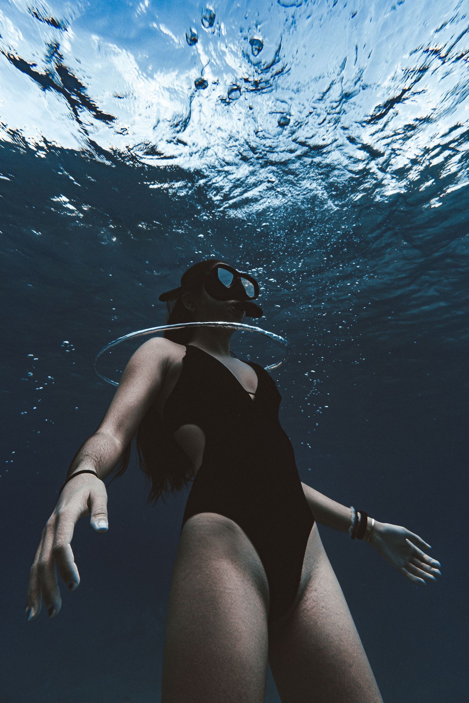 Underwater photo of a woman in a black swimsuit and diving mask with a bubble ring around her neck.