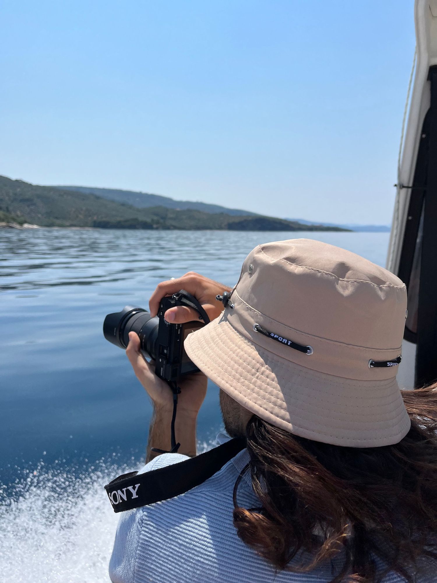 Woman in bucket hat photographs ocean scenery with Sony camera from a moving boat.