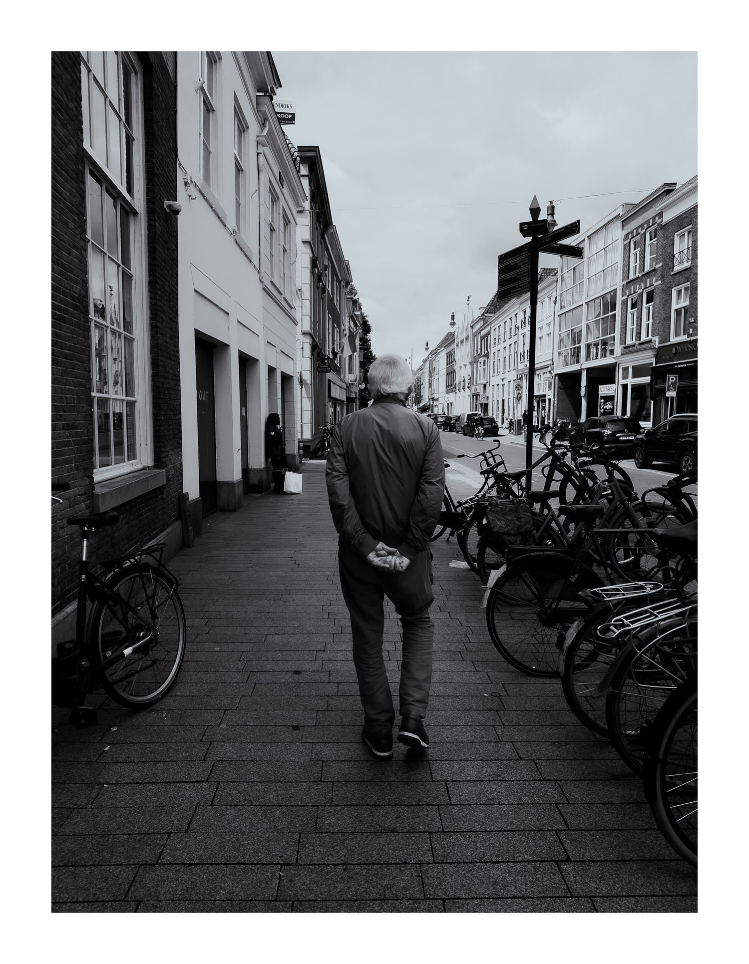 Man walking along bicycle-lined cobblestone street in European city, black and white photo.