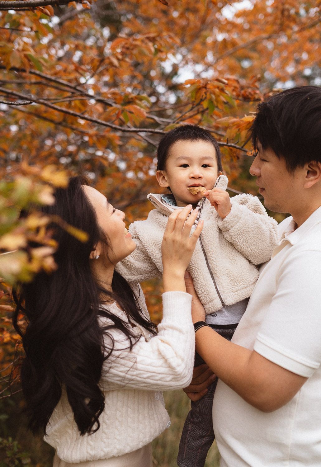 Nahaufnahme einer Familie bei einem herbstlichen Familienshooting, während der kleine Sohn ein Blatt in der Hand hält.
