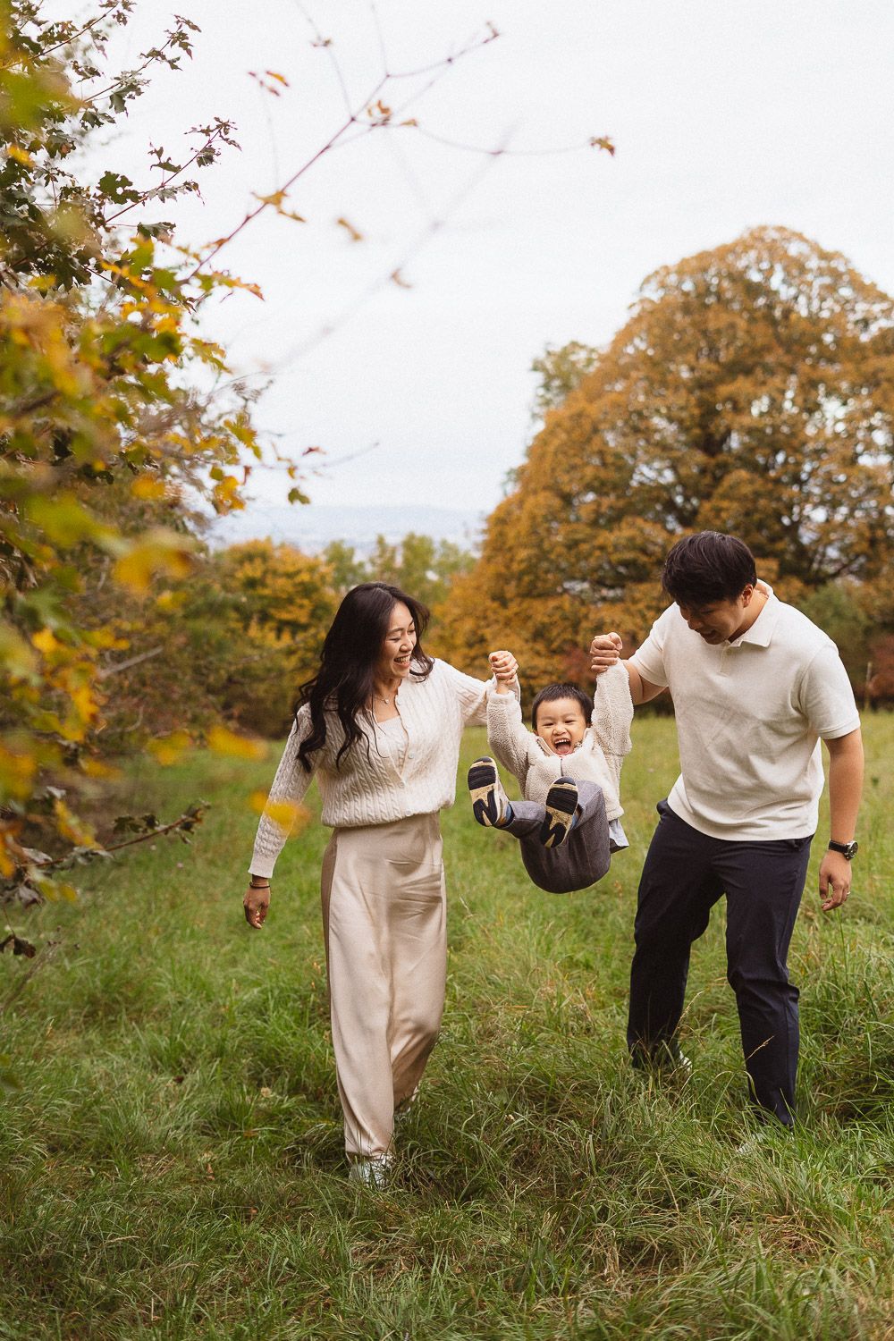 Eltern schwingen ihren Sohn beim herbstlichen Familienshooting lachend an den Händen.