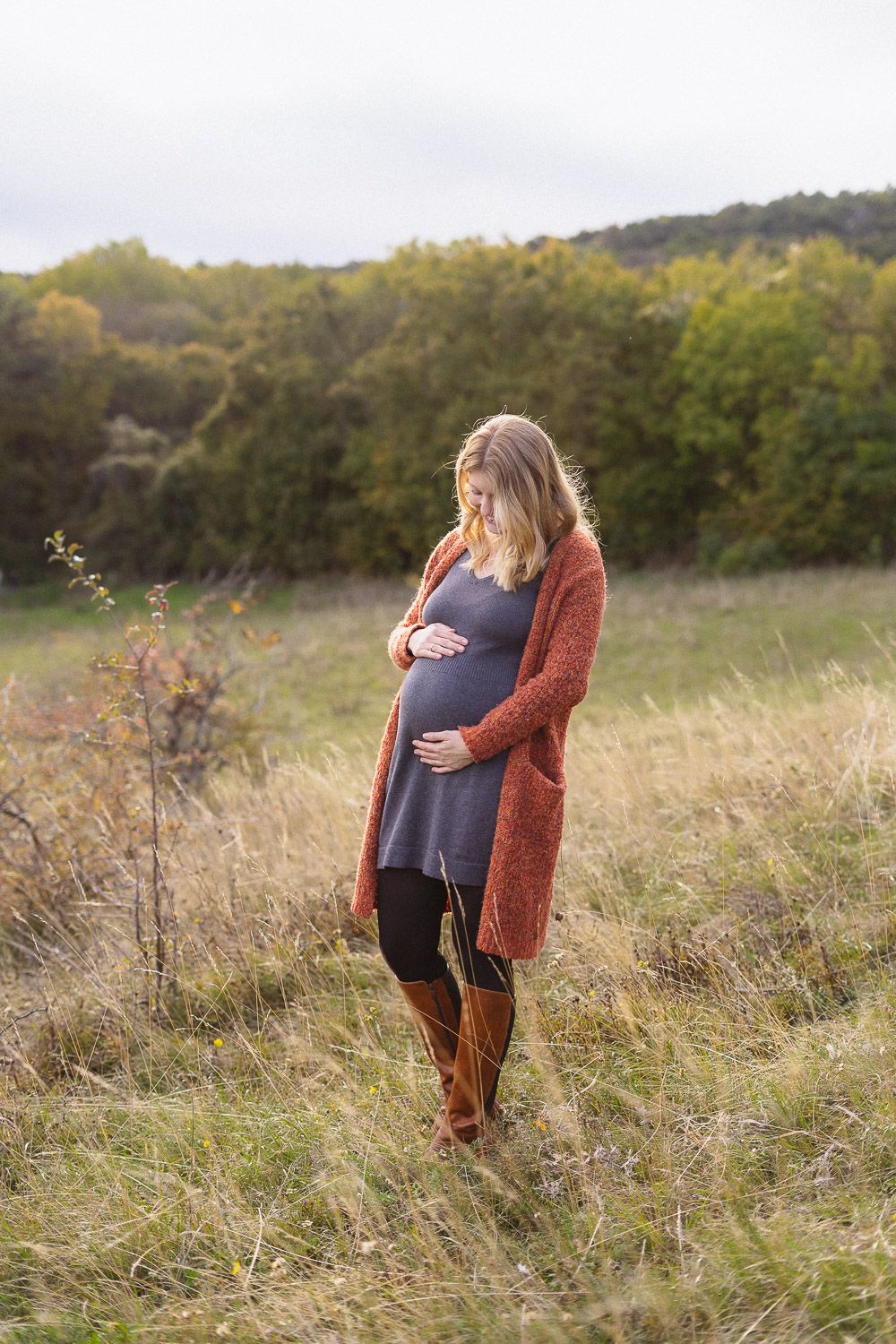Schwangere Frau hält ihren Babybauch und blickt im warmen Abendlicht zu ihm hinab.
