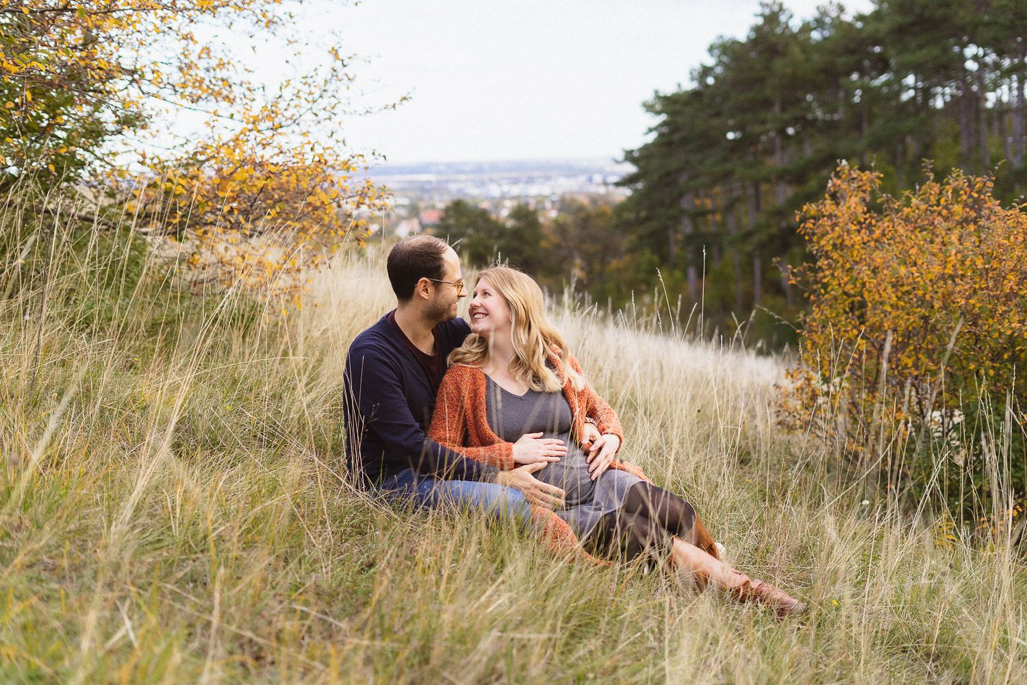 Werdende Eltern beim Babybauchshooting auf der Perchtoldsdorfer Heide, entspannt auf einer Wiese sitzend.