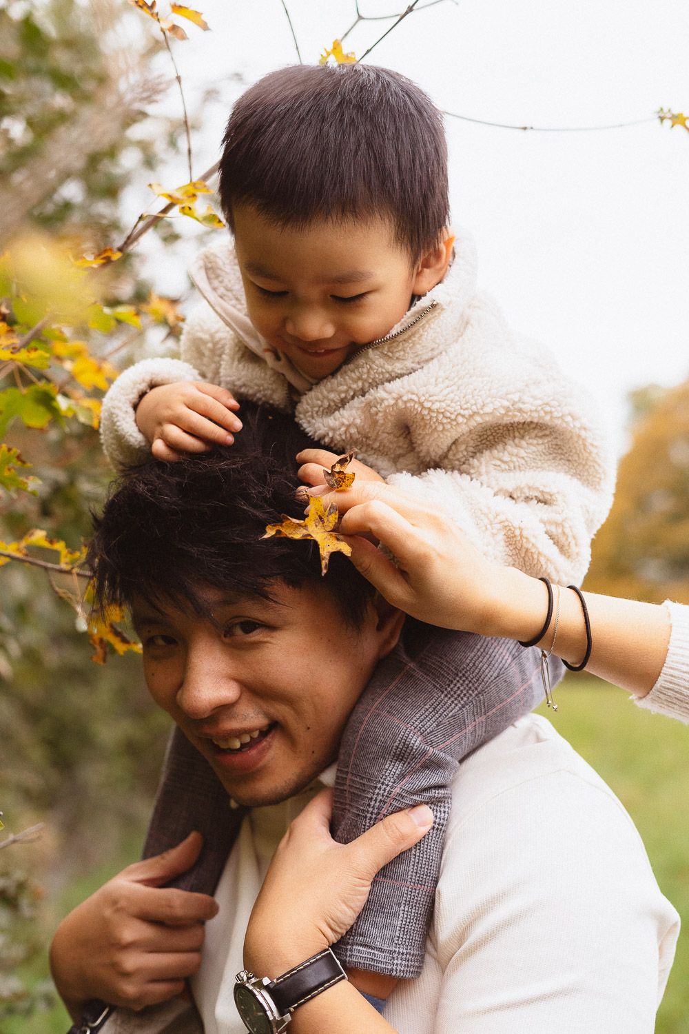Vater trägt seinen Sohn bei einem Familienshooting im Herbst auf den Schultern, während der Junge ihn ansieht.