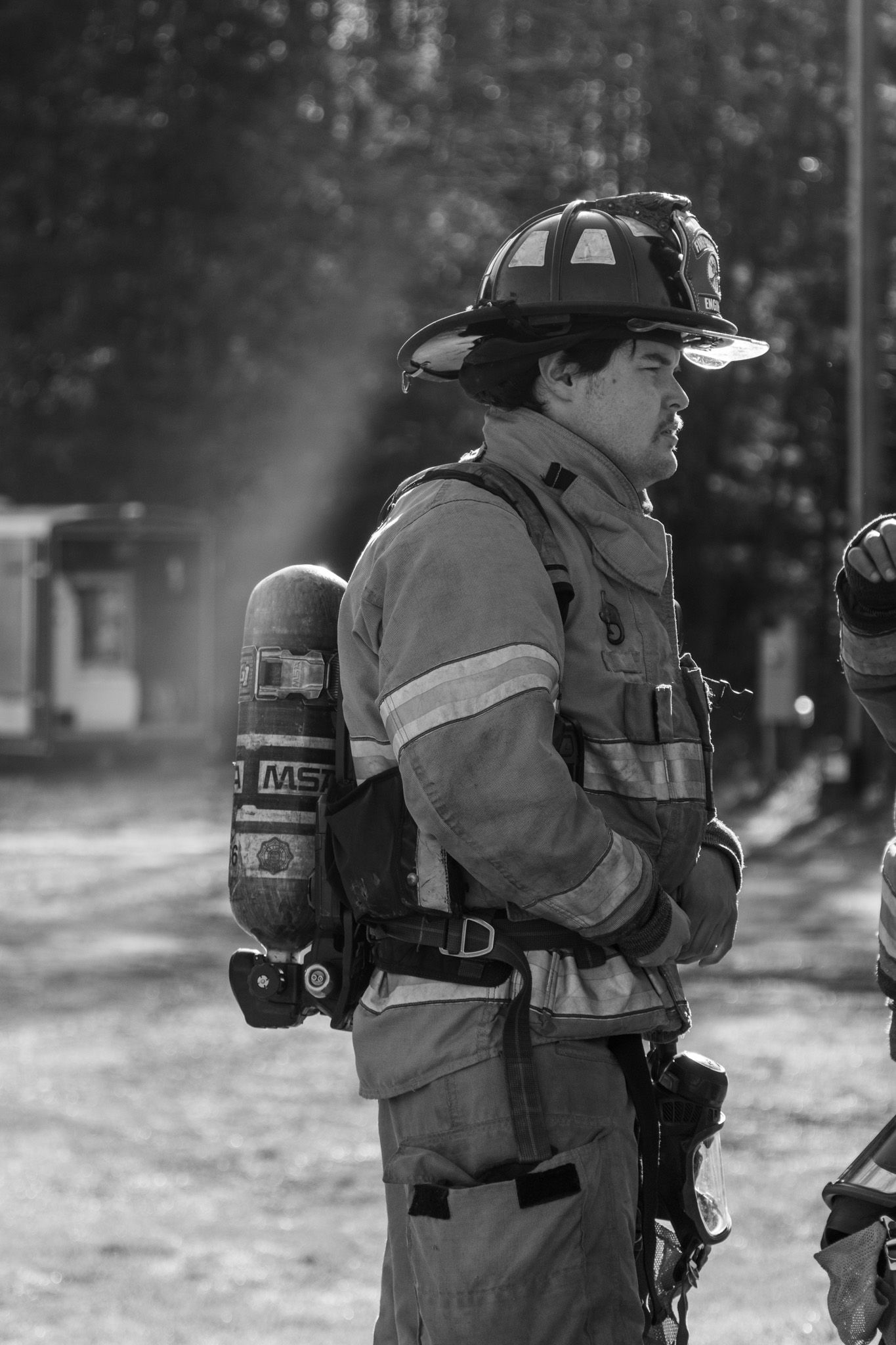 Black and white photo of a firefighter in full gear with SCBA tank standing alert outdoors.