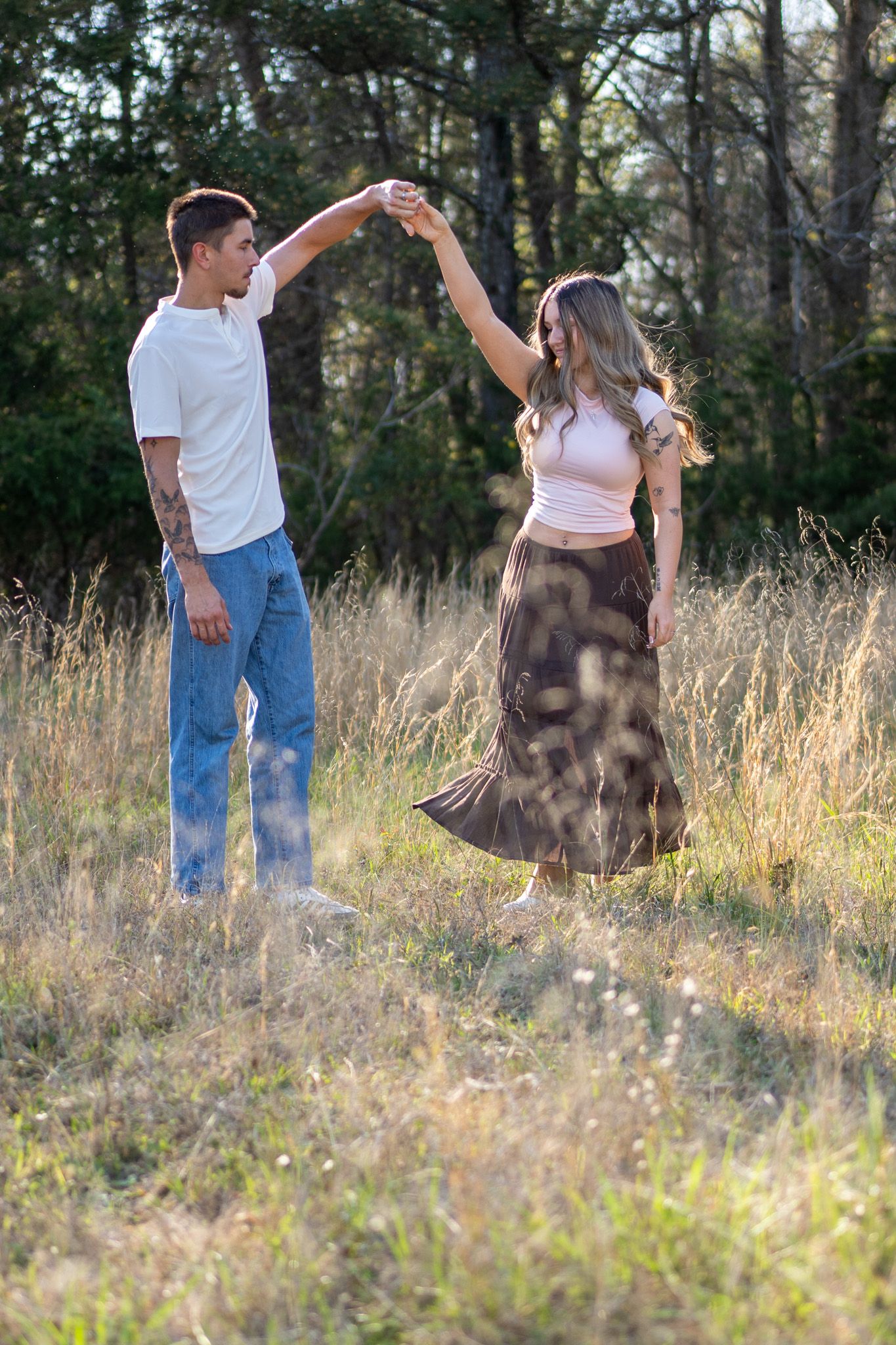 Young couple dancing together in golden sunlit field at sunset.