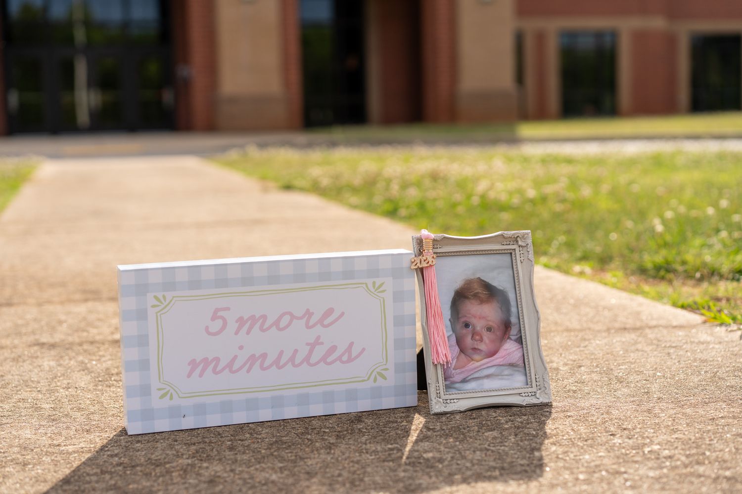 Baby photo in silver frame beside a '5 More Minutes' sign displayed outdoors on a sunny day.