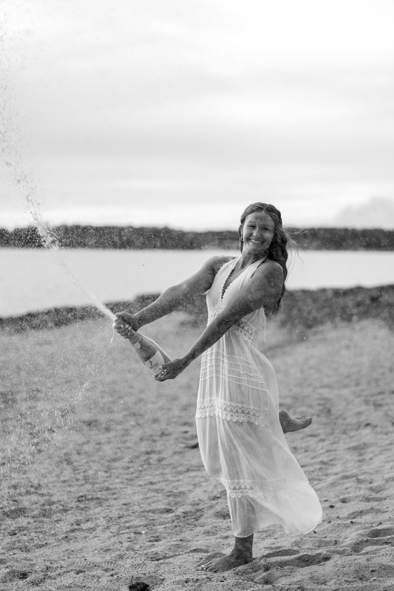 Joyful woman in white dress splashing water on a beach in a black and white portrait.