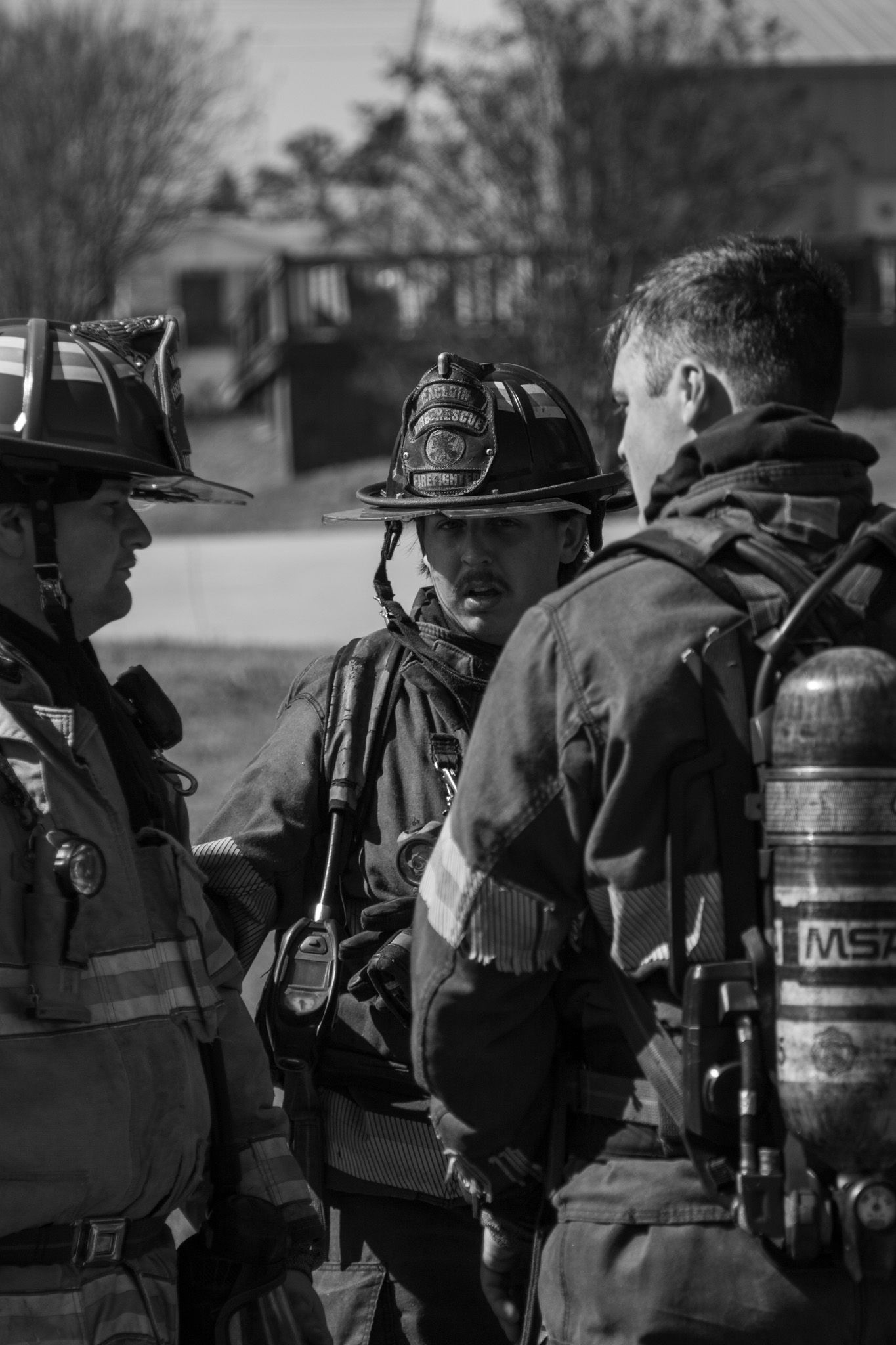 Three firefighters in full gear having a discussion at an emergency scene in black and white.