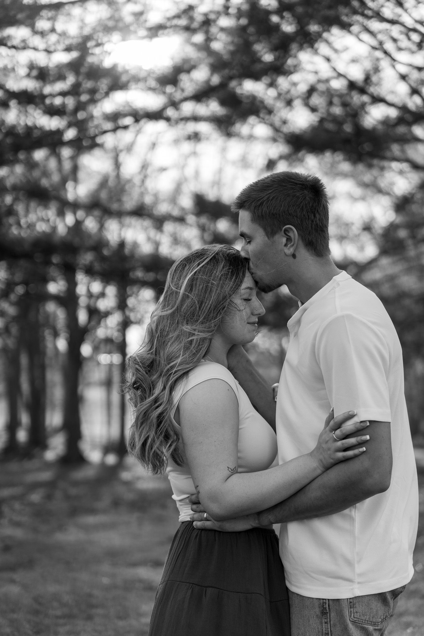 Black and white photo of romantic couple embracing in a forest at sunset.