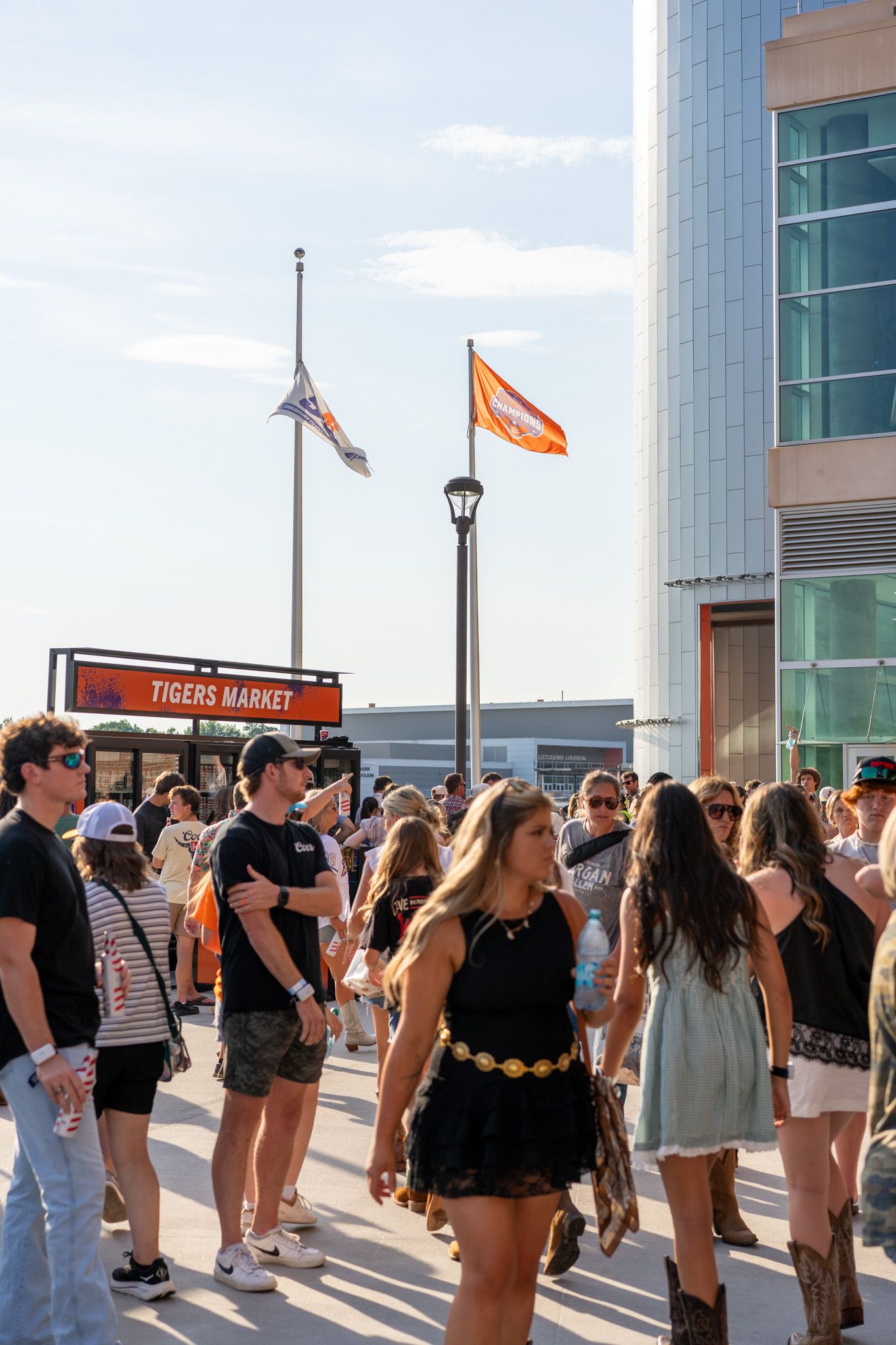 Crowd of fans gathering outside Tigers Market stadium on a sunny day with orange flags flying.