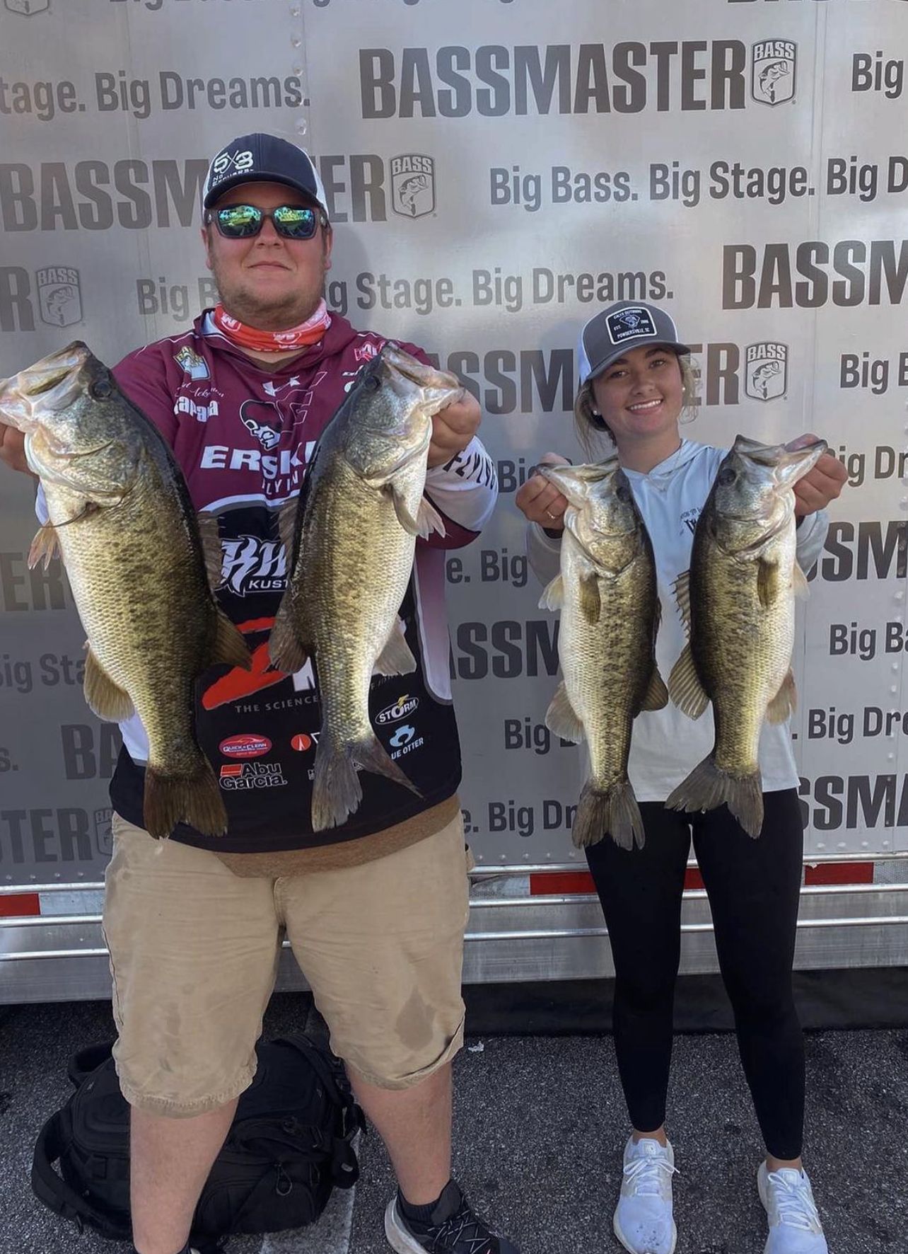 Two anglers proudly display large largemouth bass catches at a Bassmaster fishing tournament event.