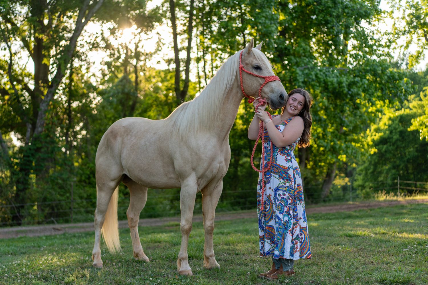 Woman in floral maxi dress affectionately bonding with a white palomino horse outdoors.