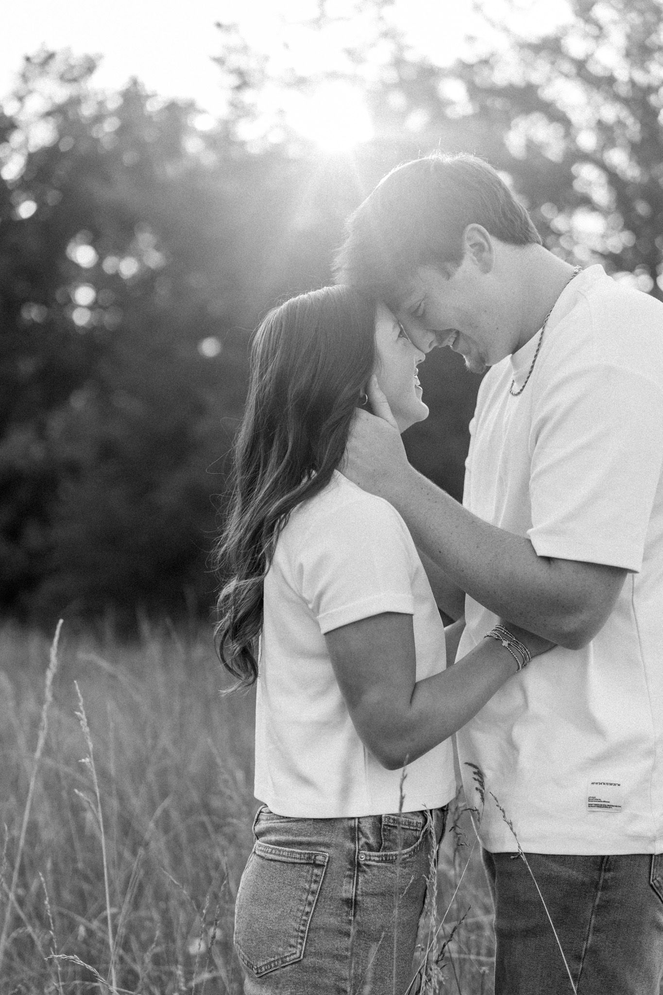 Black and white romantic portrait of couple embracing face-to-face in a sunlit meadow.