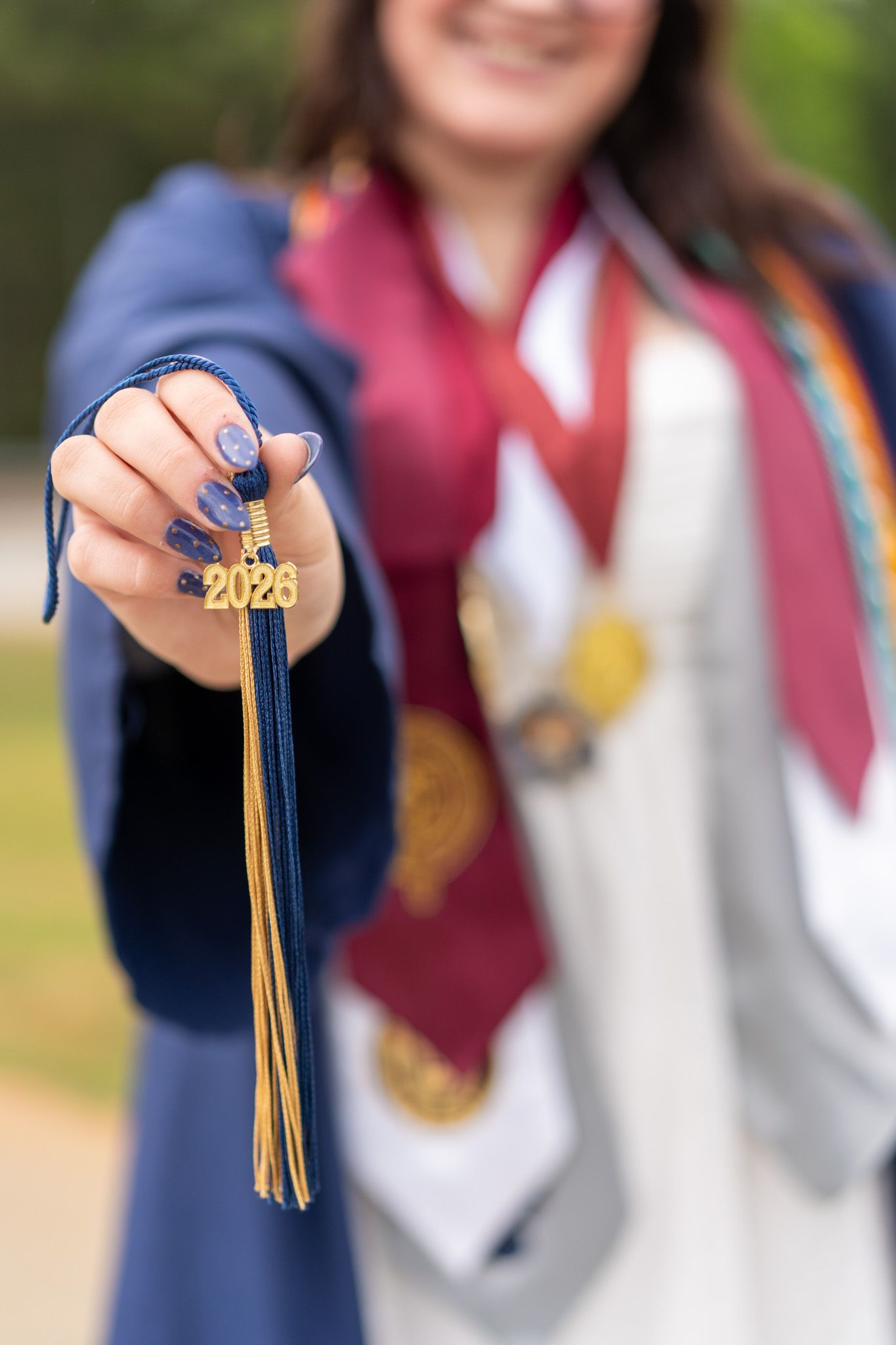 Close-up of graduate holding 2026 tassel toward camera in navy and gold graduation regalia.