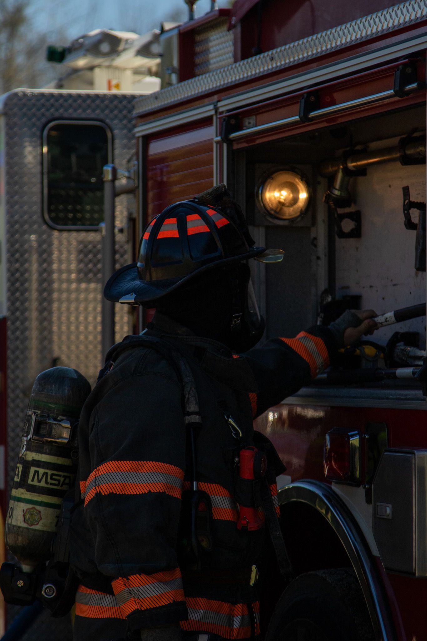 Firefighter in full gear with MSA breathing apparatus stands beside a red fire truck during an emergency response.