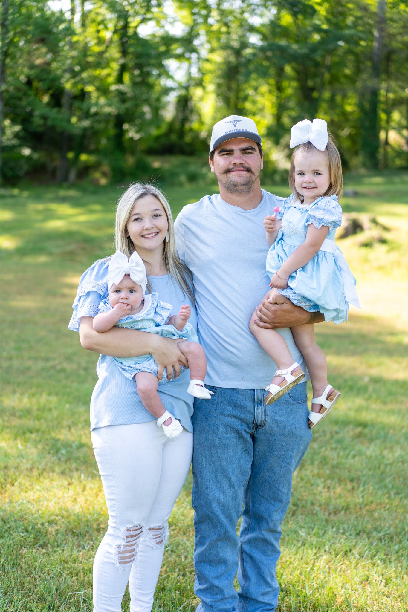 Happy family of four in matching blue outfits posing outdoors in a sunny green park.
