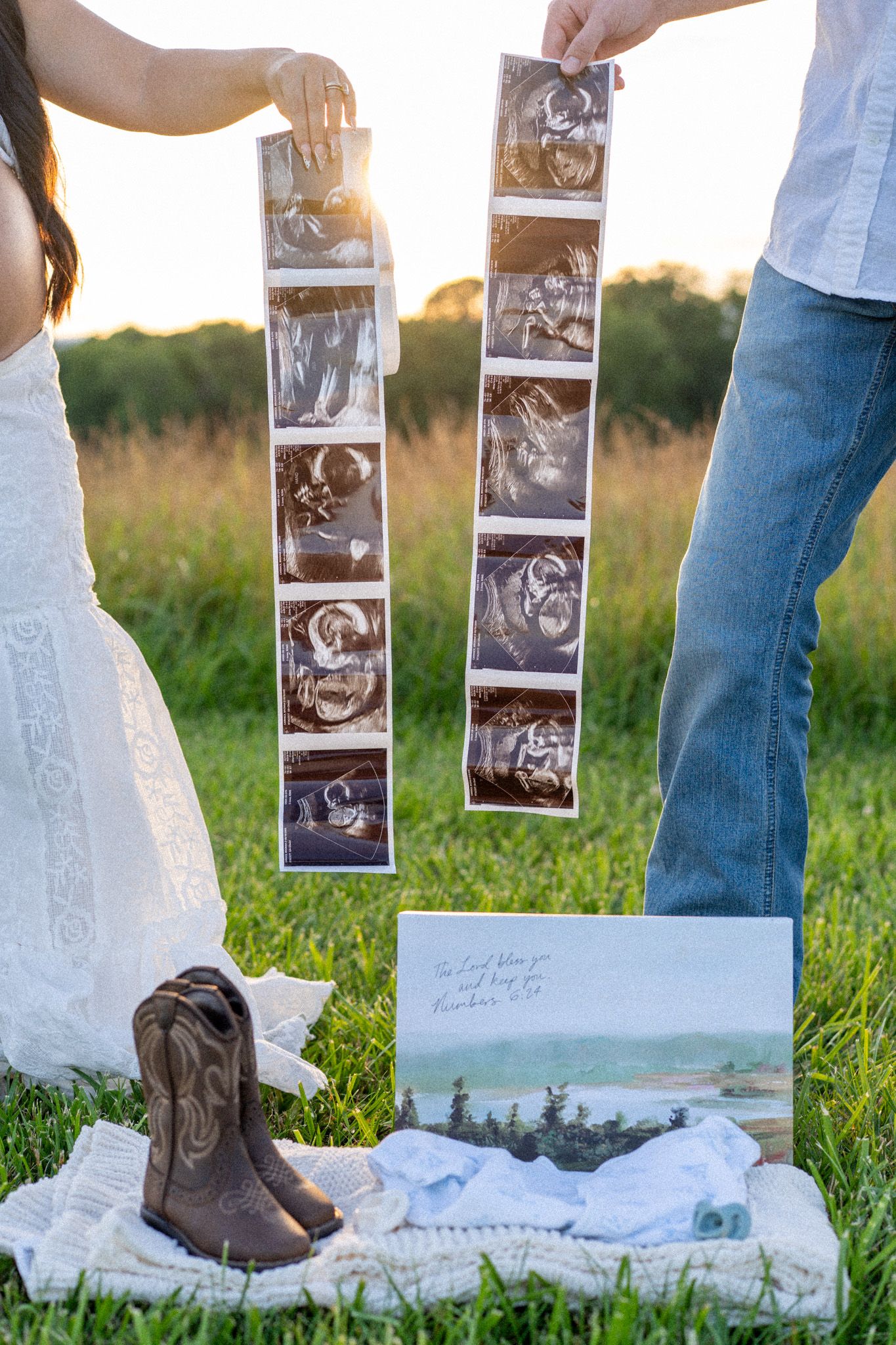 Couple holding ultrasound strips outdoors with baby boots and a card on a blanket below.
