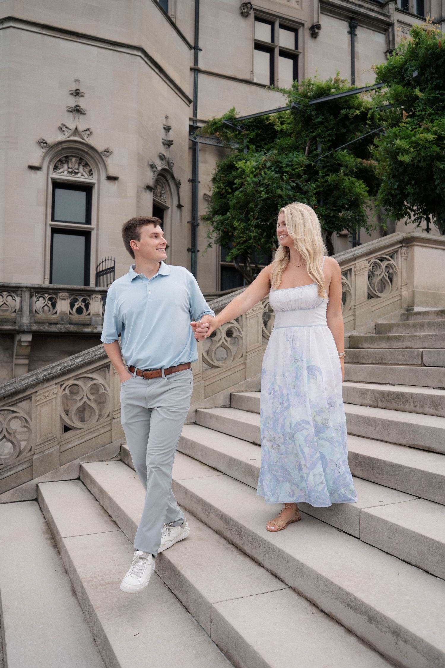 Happy couple holding hands while descending ornate stone steps of a historic mansion.